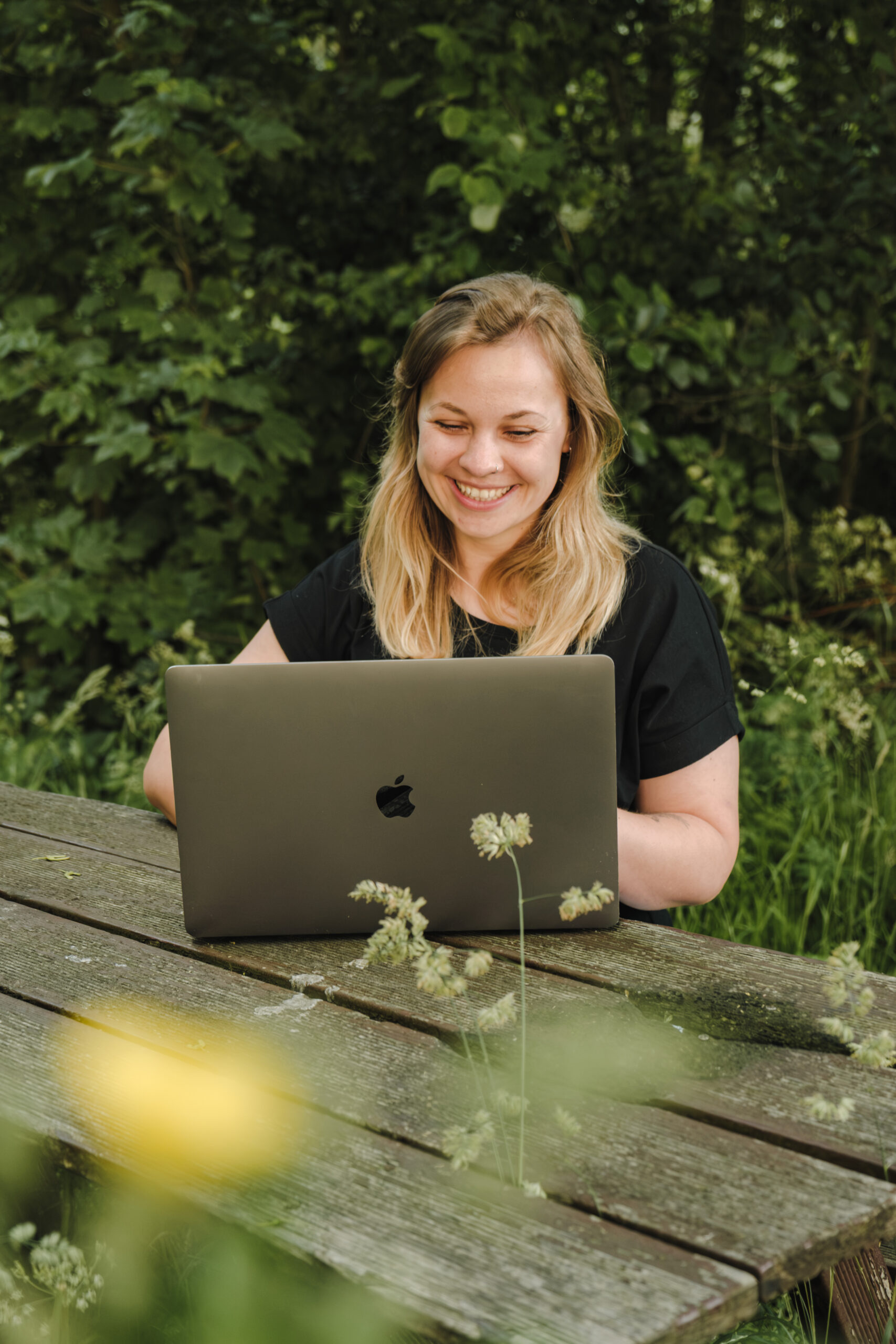 Miriam Kaczmarzik sitzt an einer Picknickbank im Wald an ihrem MacBook