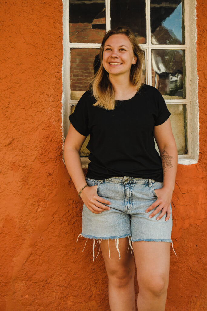 Miriam lehnt an einer Orangenen Mauer